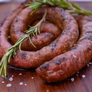 A spiral-shaped grilled Brêkfis Boerewors sausage on a wooden board, garnished with rosemary and sea salt