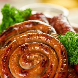 Grilled Hot Masala Lamb Sausage coiled on a platter with herbs, spicy South African Indian-style sausage