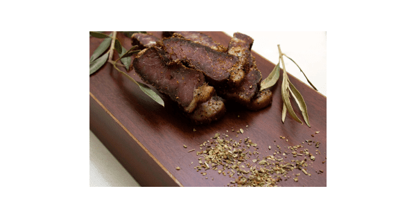 Bobaas premium sliced biltong pieces on wooden cutting board with coriander seeds and eucalyptus leaves, authentic South African air-dried beef snack